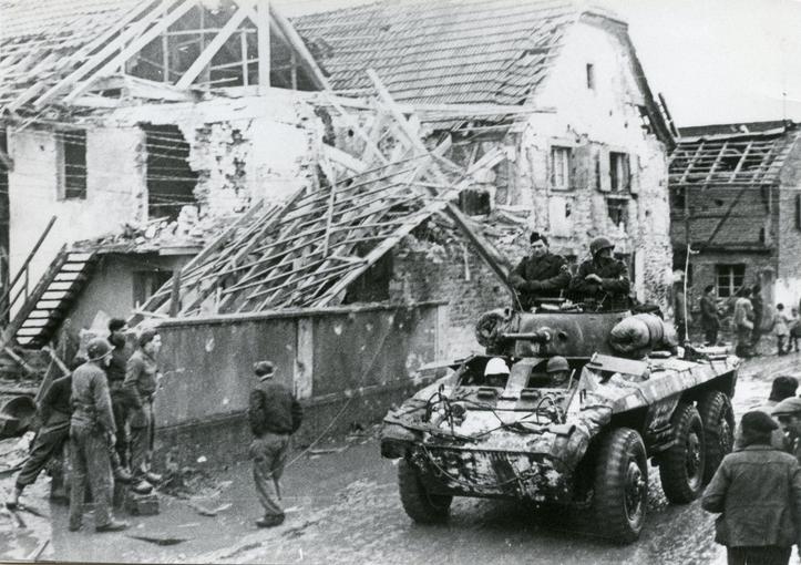 Des soldats américains sur un char traversant Sélestat  dont plusieurs quartiers sont en ruines. 