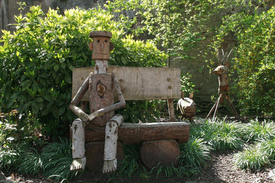 Un bonhomme en bois sur un banc dans le jardin des Dahlia